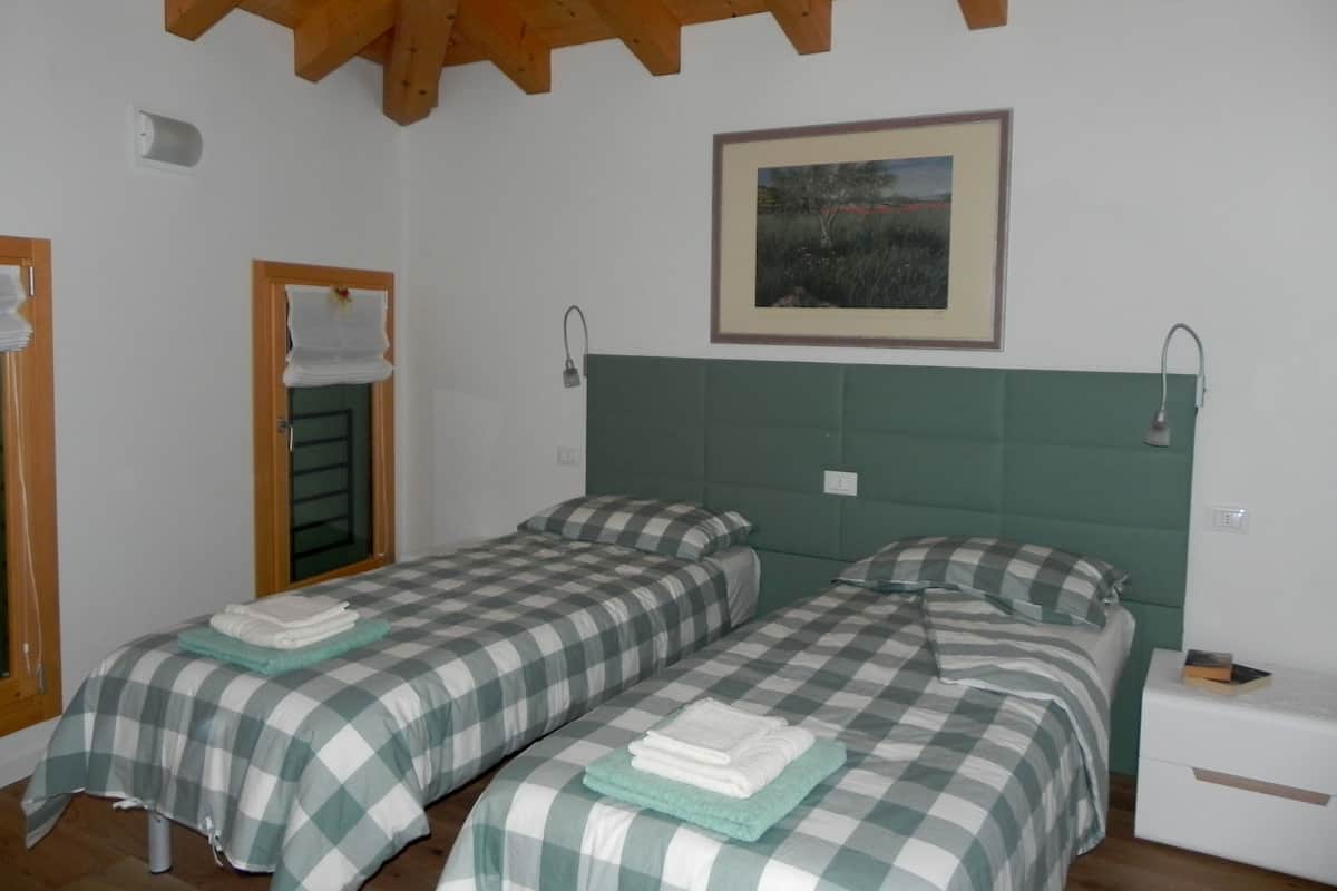 Een kamer met twee bedden, elk voorzien van een geruit sprei en kussens. Daarboven hangt aan de muur een ingelijst schilderij, en bij elk bed staat een klein nachtkastje met een lamp. Het plafond is van hout.
