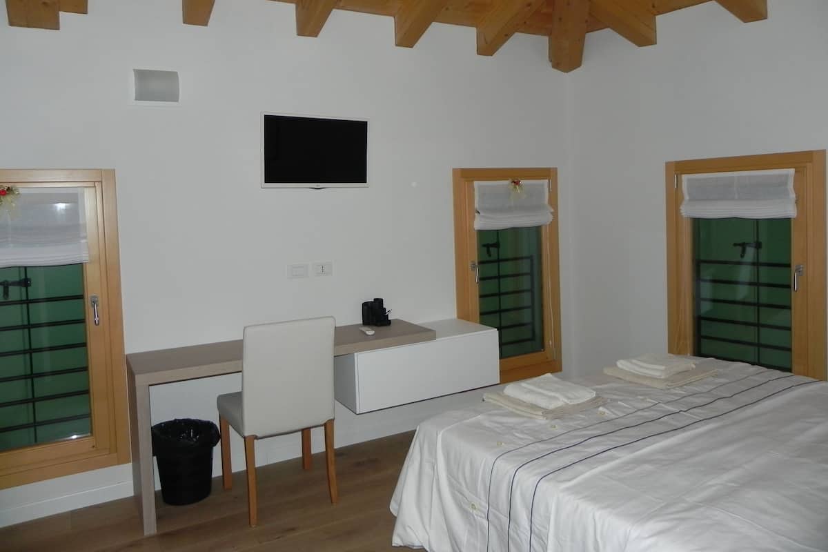 Een slaapkamer met een bed, een bureau, een stoel, een televisie en twee deuren met groene glaspanelen.