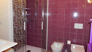 A bathroom with a glass-enclosed shower, a bidet, and a toilet.