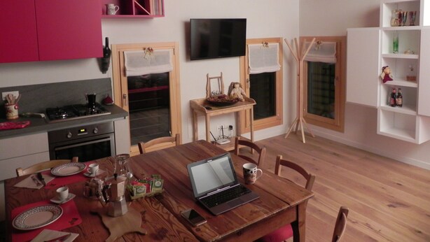 A cozy kitchen with wooden beams, a dining table with chairs, a laptop, and a TV mounted on the wall. - da Meri Locazione Turistica Appartamento (Farra di Soligo)
