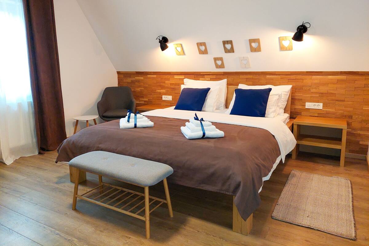 A hotel room with a wooden headboard, a bed with blue and white bedding, a bench, and a small bedside table.
