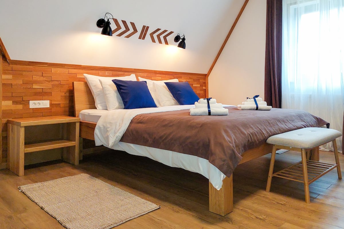 A modern bedroom with a wooden headboard, a bed with white and blue bedding, a bedside table, a bench, and a woven rug.