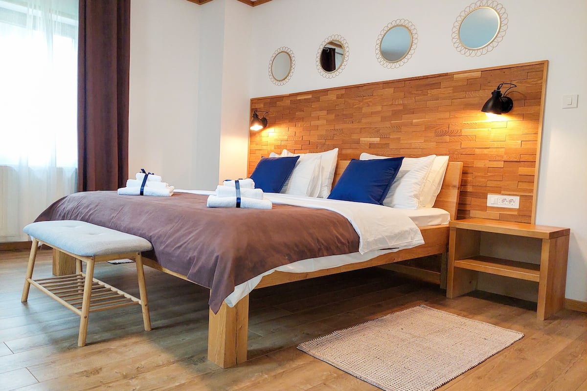A bedroom with a wooden headboard, a bench at the foot of the bed, and a bedside table with a lamp.