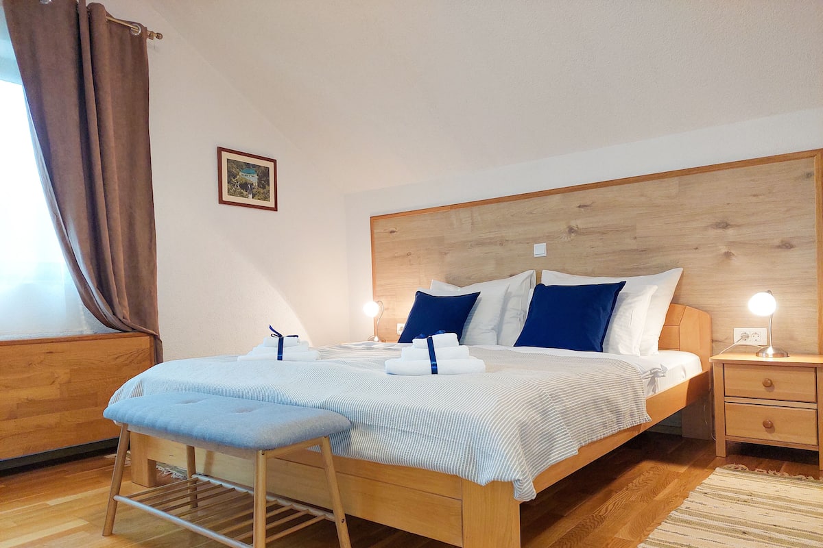 A neatly made bed with blue and white pillows, a wooden headboard, a bedside table with a lamp, and a small bedside table with a lamp.