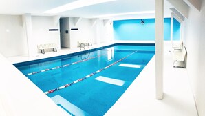 A modern indoor swimming pool with clear lane dividers, a blue wall, and a bench along one side. - Apartment Downtown 3 K (Mexico City)