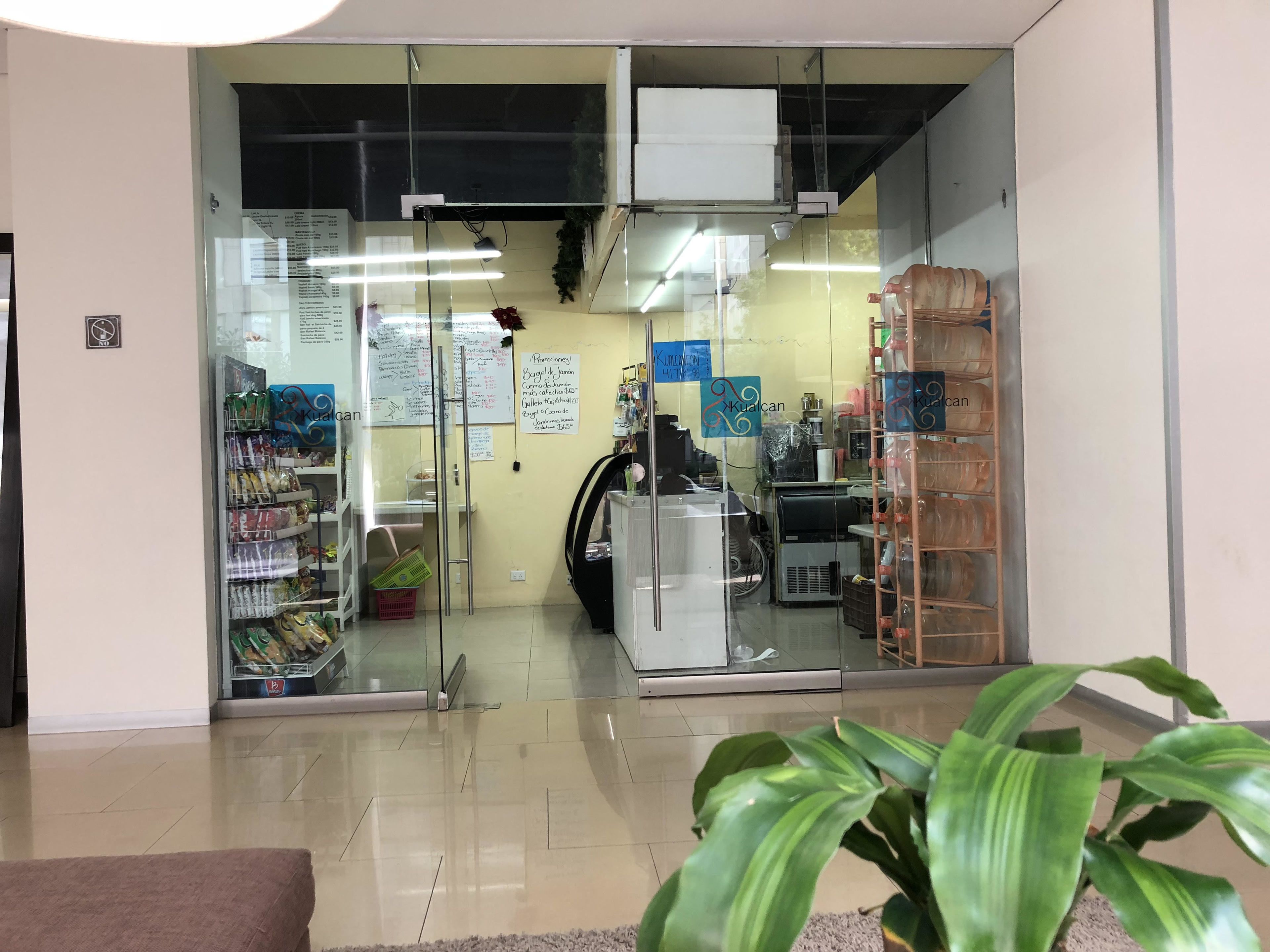 Una tienda con puertas de cristal, estantes llenos de productos y un mostrador a la vista.