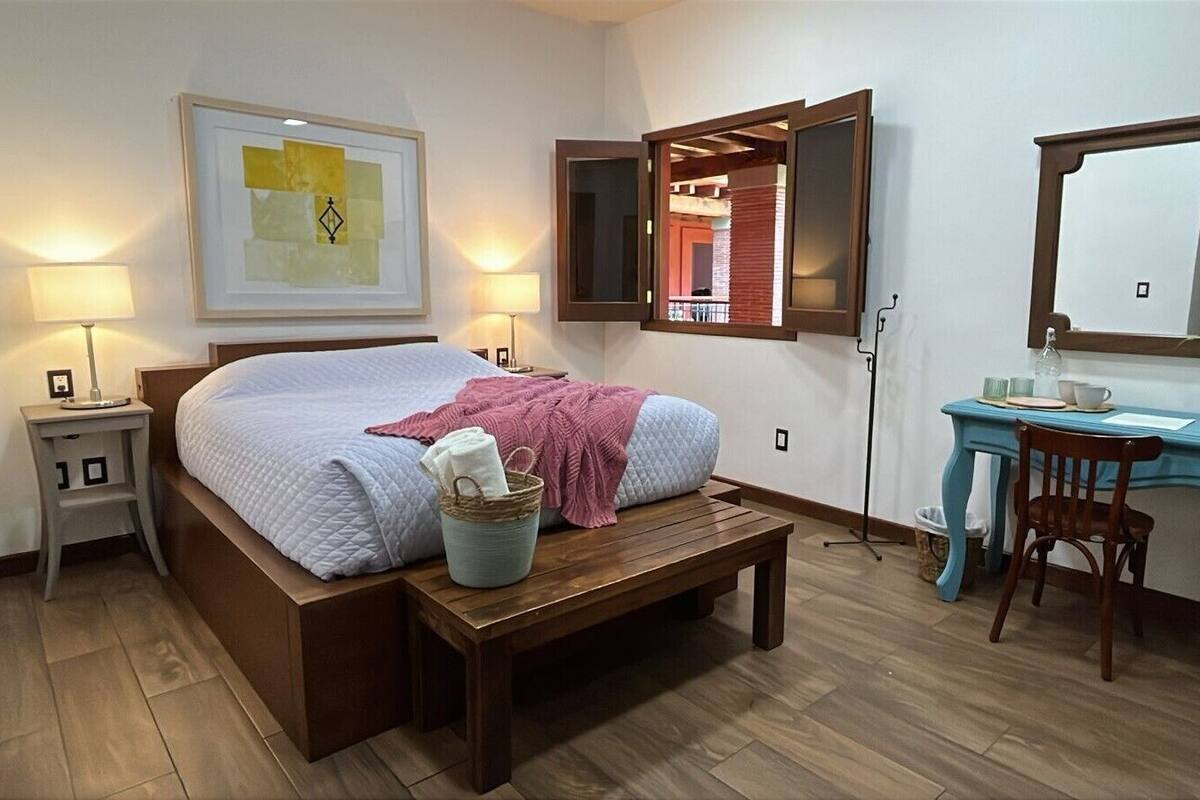 Ein Schlafzimmer mit Bett, Nachttischen, Schreibtisch, Stuhl, Spiegel und Fenster.
