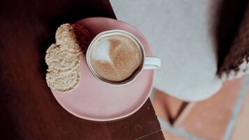 A cup of coffee on a pink saucer with biscotti on a wooden table.