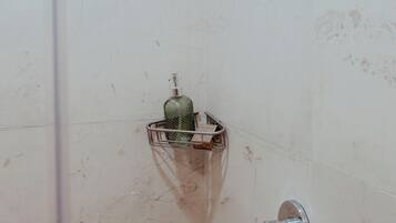 Une douche équipée d’un pommeau de douche à main, d’une étagère en verre sur laquelle est posée une bouteille, et d’un robinet en métal.