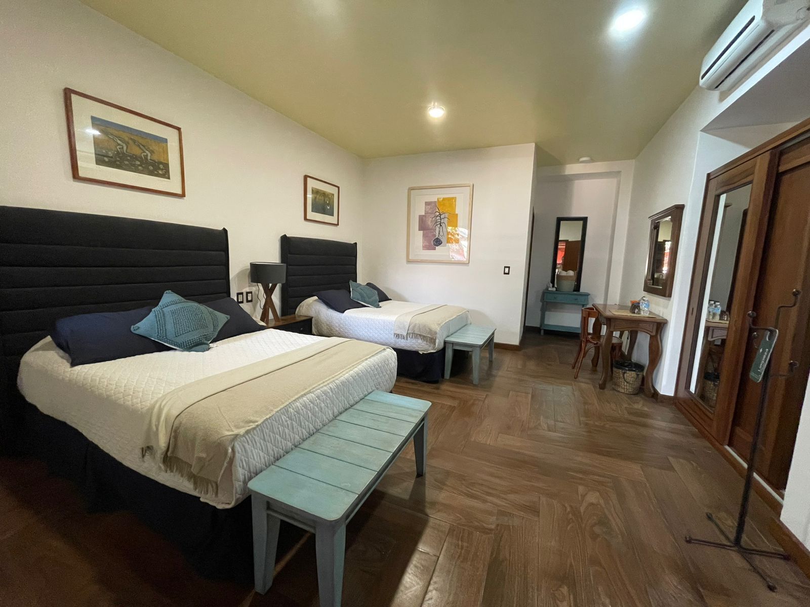 Una habitación de hotel con dos camas, un banco, un escritorio y un espejo.