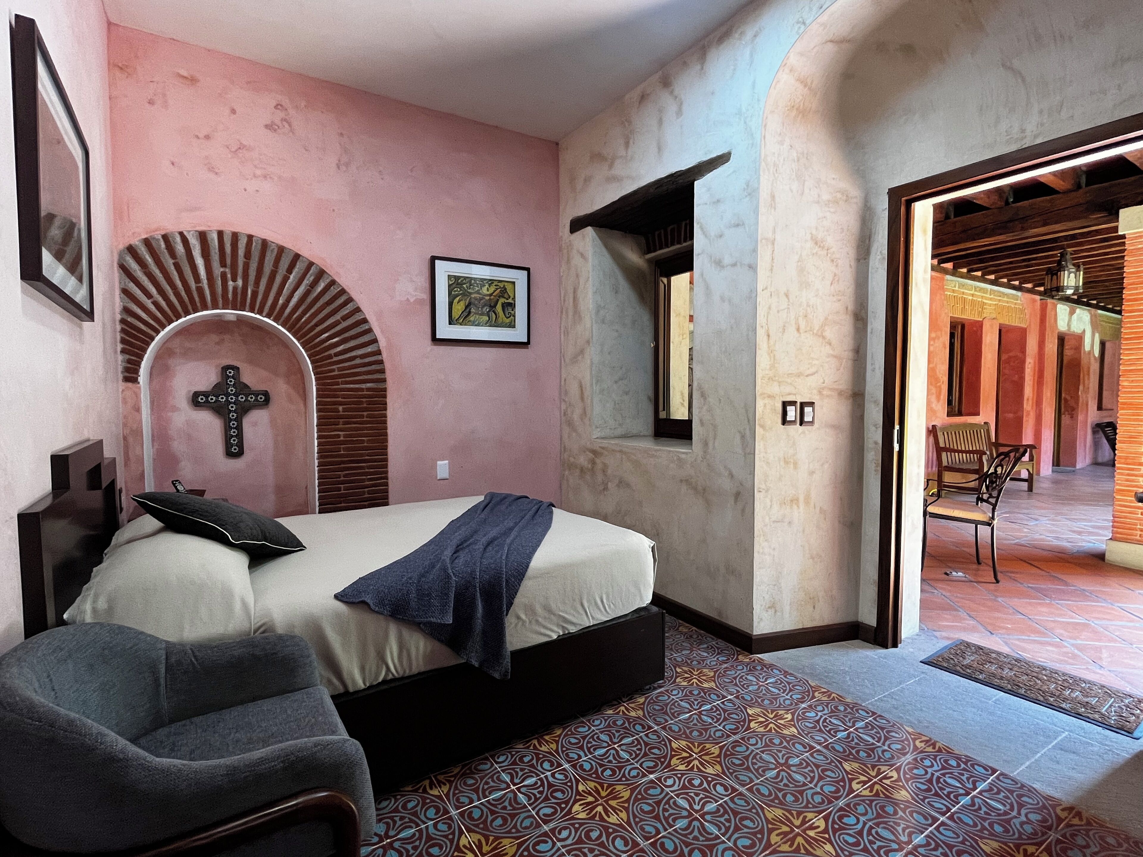 A bedroom with a bed, a cross on the wall, and a door leading to another room.