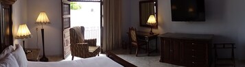 Quarto de hotel com uma cama, duas luminárias de cabeceira, uma escrivaninha com cadeira, um guarda-roupa e uma televisão.