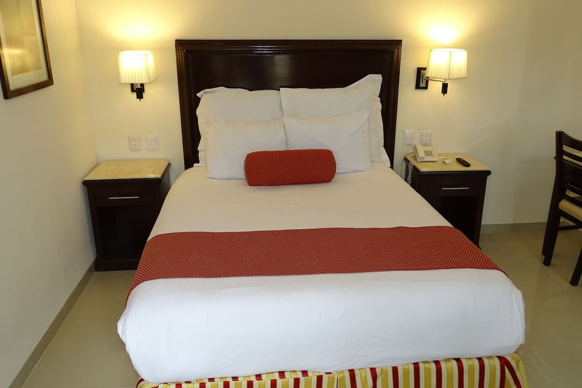 A hotel room with a large bed, two bedside tables, a desk, and a chair.
