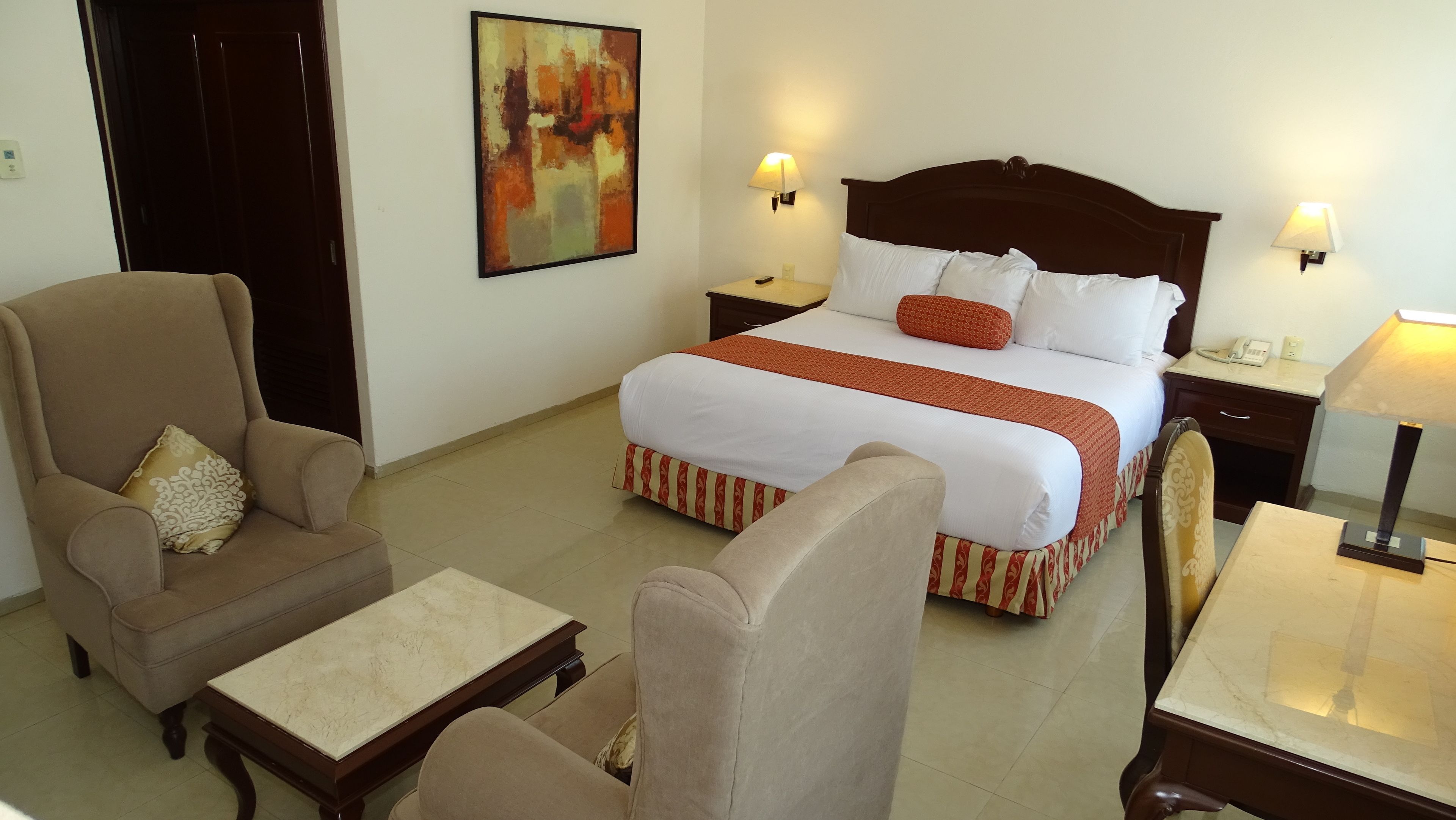 Une chambre d’hôtel comprenant un lit, deux fauteuils, une petite table et une table de chevet avec une lampe.