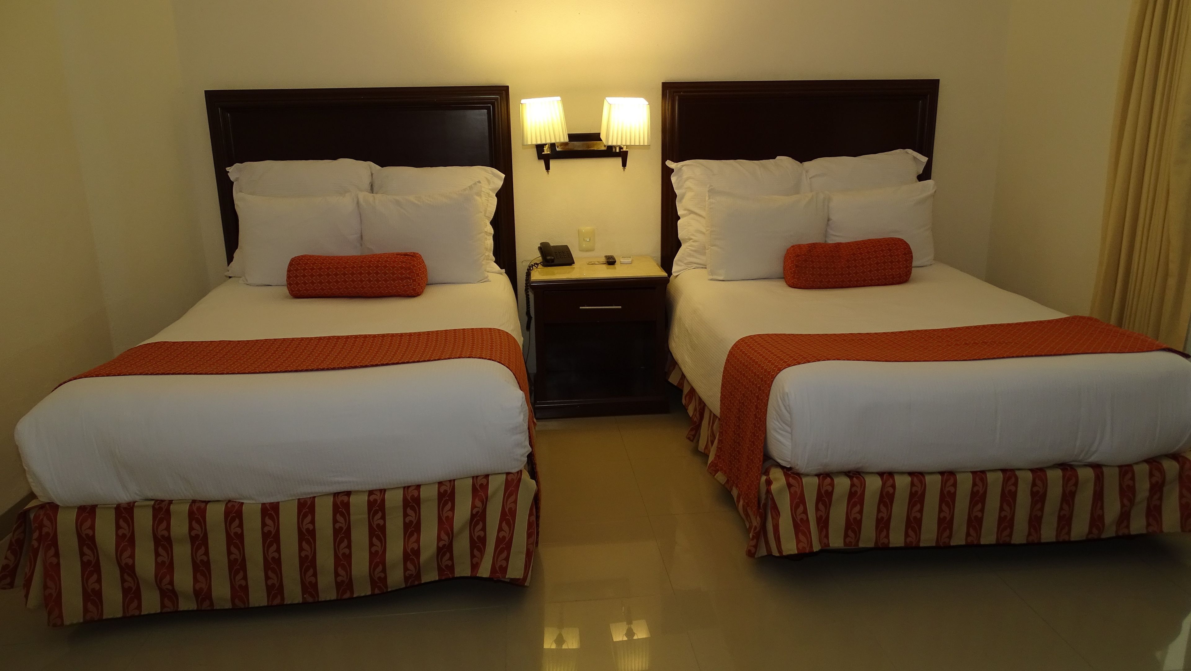 Habitació d'hotel amb dos llits, cadascun amb roba de llit blanca i detalls vermells, una petita taula de nit amb una làmpada i un telèfon.