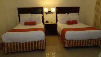 Habitació d'hotel amb dos llits, cadascun amb roba de llit blanca i detalls vermells, una petita taula de nit amb una làmpada i un telèfon.