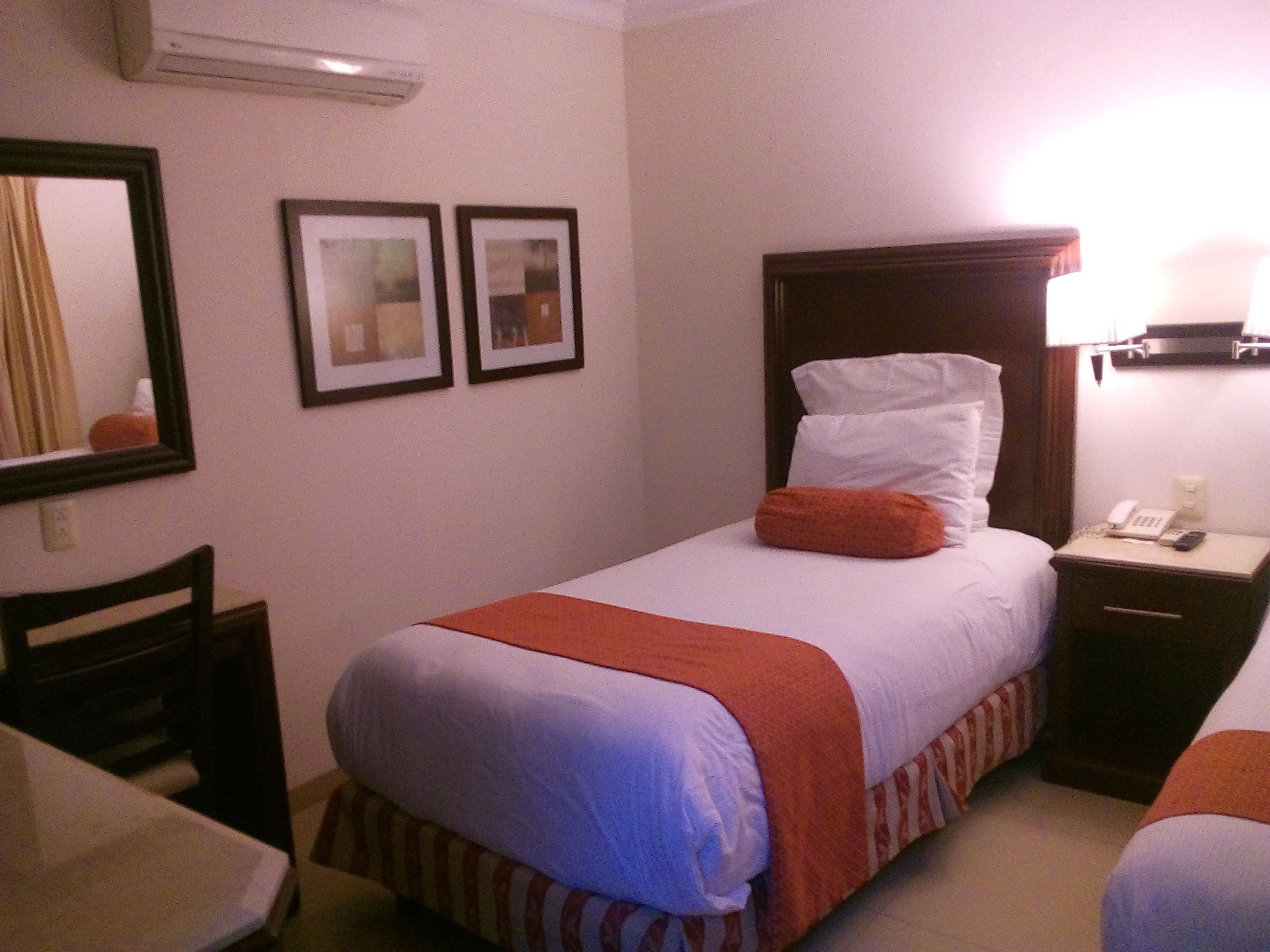 A hotel room with a bed, a nightstand with a phone, a chair, and two framed pictures on the wall.