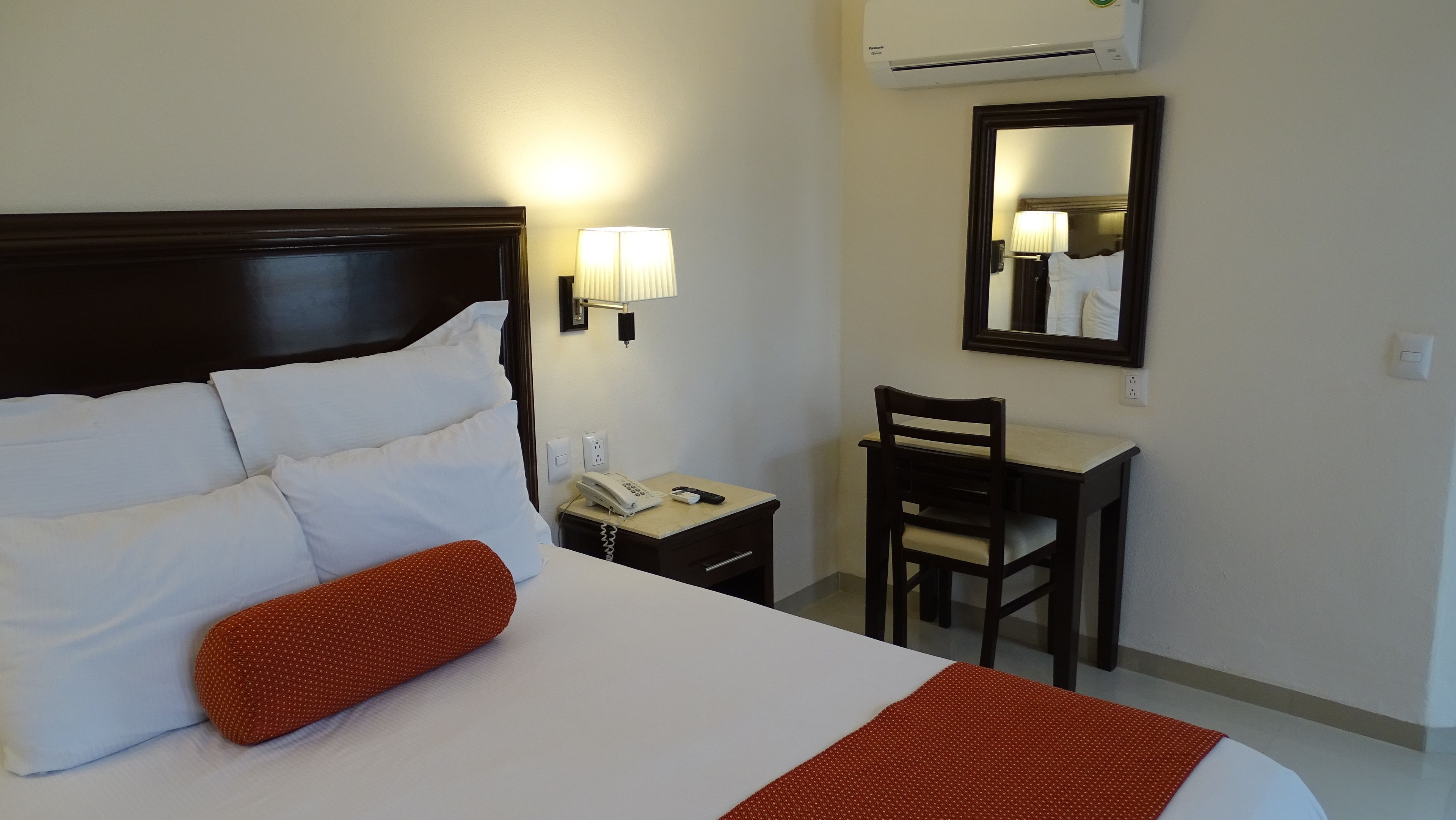 A hotel room with a large bed, a desk, a chair, a telephone, and a mirror.