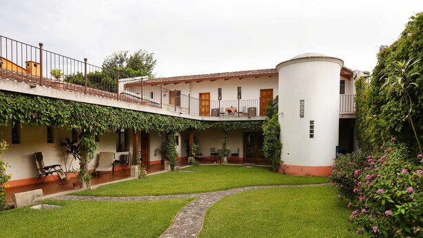 Un patio con un edificio blanco, un camino de piedra y una pequeña zona ajardinada.