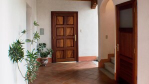 Un pasillo con puerta de madera, suelo de baldosas y plantas en macetas.