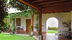 Un patio cubierto con piso de baldosas, un pequeño césped y un espacio de estar con una mesa y sillas.