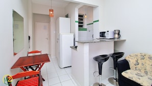 A compact kitchen with a refrigerator, a coffee maker, and a microwave. There is a dining table with chairs and a bar stool. - MZapartments Bulhoes (Rio de Janeiro)