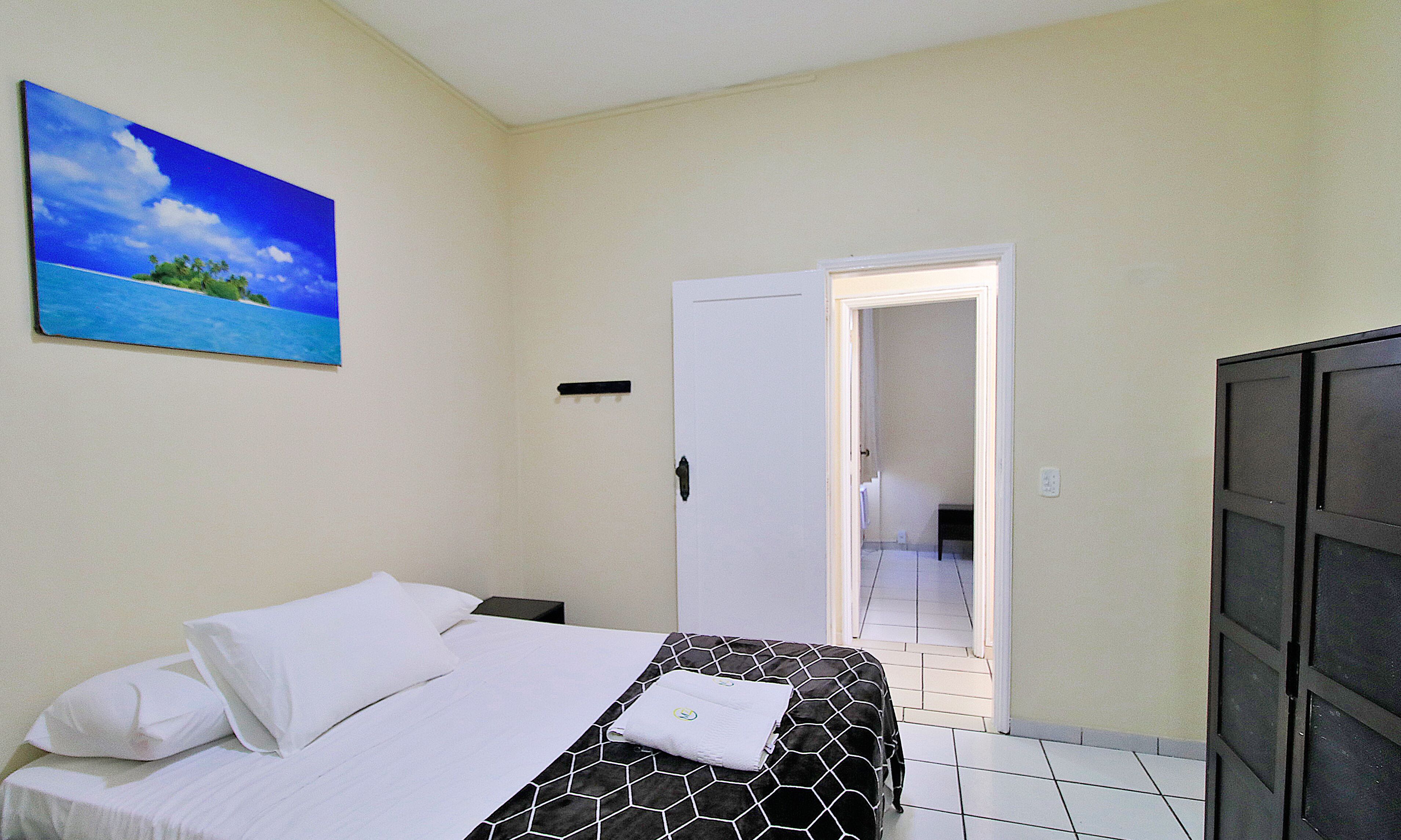 Una habitación de hotel con una cama, un cuadro de una playa y una puerta que da a otra habitación.