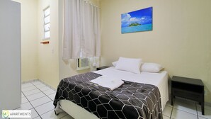 A bedroom with a bed, a nightstand, a painting of a beach, a window with curtains, and a radiator. - MZapartments Djalma (Rio de Janeiro)