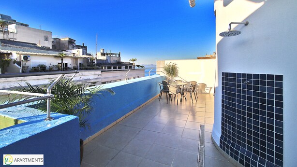 A rooftop terrace with a blue wall, a tiled floor, and a small table with chairs. - MZapartments Djalma (Rio de Janeiro)