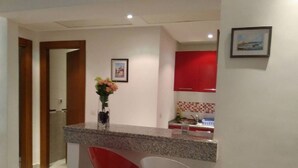 A kitchen with a granite countertop, red bar stools, and a red cabinet. - Appartement Phenix (Sousse)