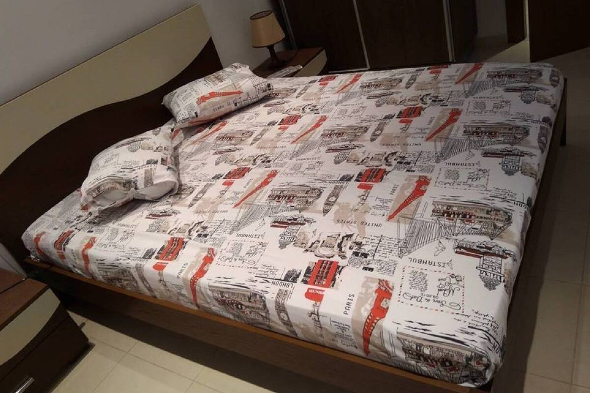 A bed with a patterned bedspread, a wooden headboard, a nightstand with a lamp, and a mirror on the wall.