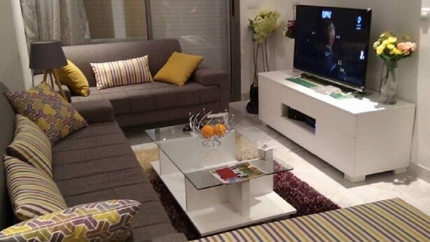 A modern living room with a sofa, a coffee table, a TV, and a small white cabinet. - Appartement Phenix (Sousse)