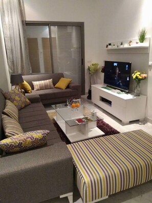 A modern living room with a sofa, a coffee table, a TV, and a white entertainment unit. - Appartement Phenix (Sousse)