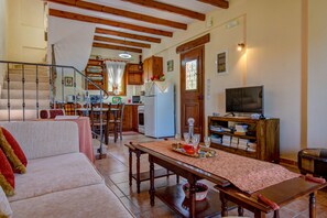 A cozy living room with a sofa, a dining table with a placemat, a kitchen area with wooden cabinets, a refrigerator, and a television on a wooden cabinet. - Sokraki Villas (Corfu)
