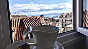 A view from a window overlooking a cityscape with terracotta rooftops and a body of water in the distance. - Villa Daky (Split)