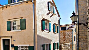 A two-story building with a beige facade, green shutters, and a stone wall adjacent to it. - Villa Daky (Split)