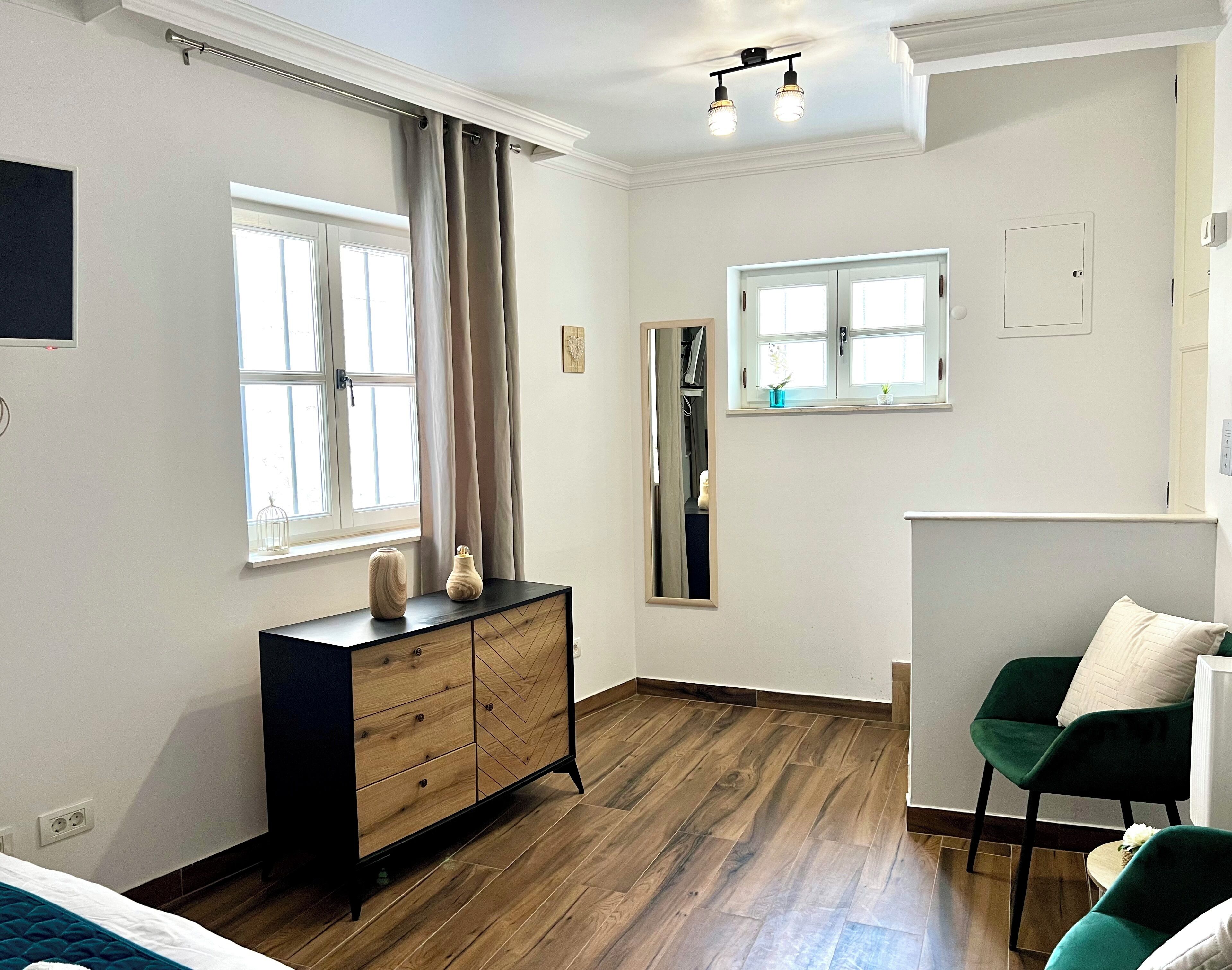 A room with a wooden dresser, a green chair, and a window with curtains.
