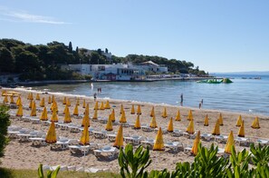 A beach with rows of sun loungers and umbrellas, a clear sky, and a building in the background. - Villa Daky (Split)