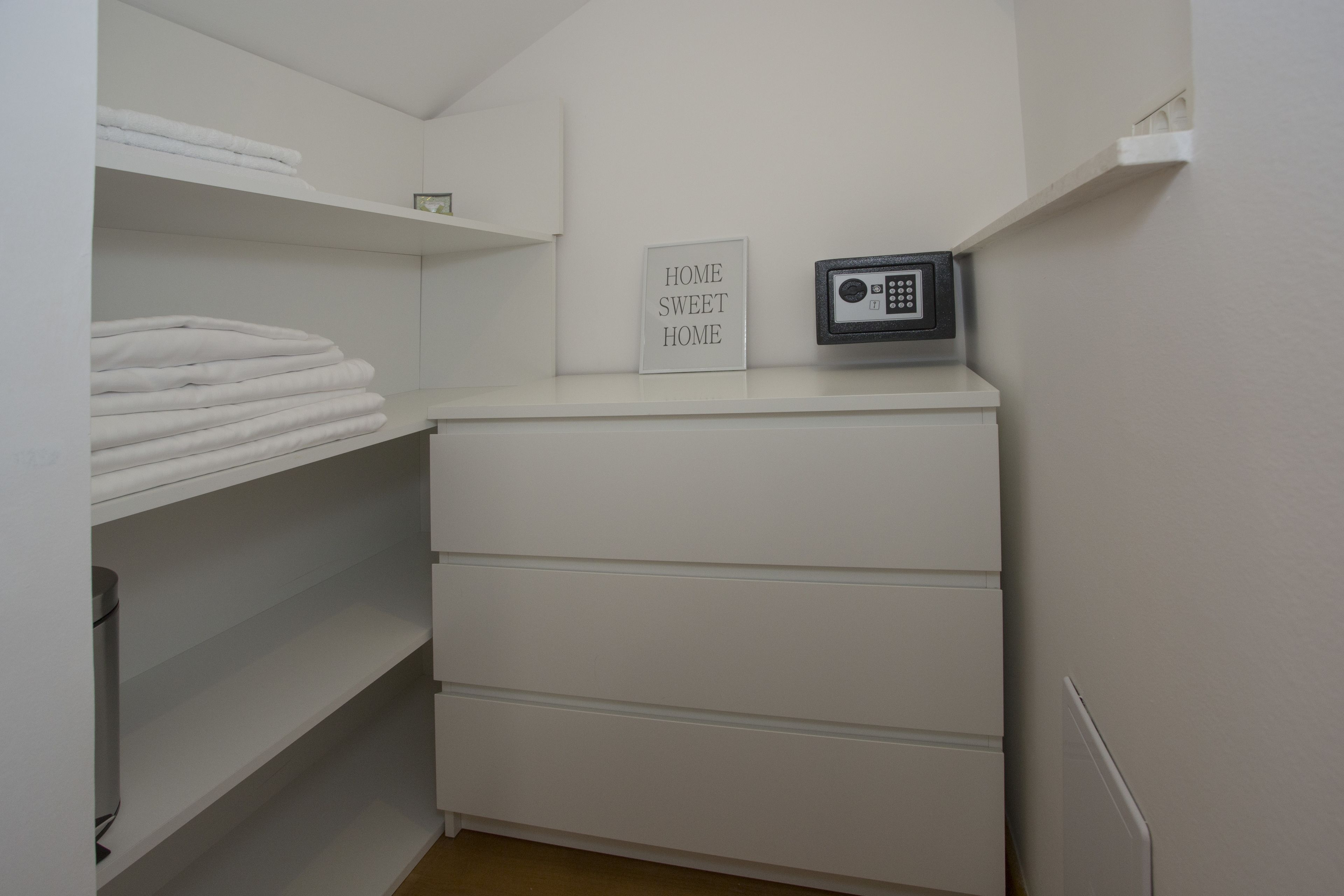 A white storage unit with shelves and a drawer, a framed sign that reads "HOME SWEET HOME," and a black security keypad.
