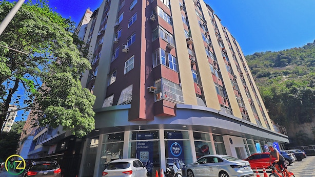 A multi-story building with a curved corner entrance, several cars parked in front, and a clear blue sky.