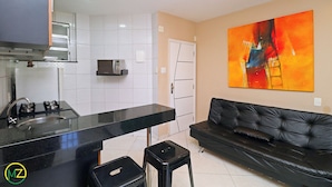 A modern kitchen with a black countertop, a stove, and a microwave. There is a black leather sofa and a colorful abstract painting on the wall.