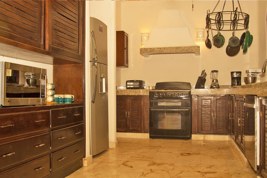 A kitchen with wooden cabinets, a stainless steel refrigerator, a microwave, a stove, and a hanging pot rack.