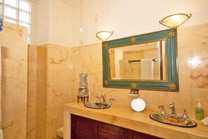 A bathroom with a marble wall, a green-framed mirror, two sinks, and a towel rack.