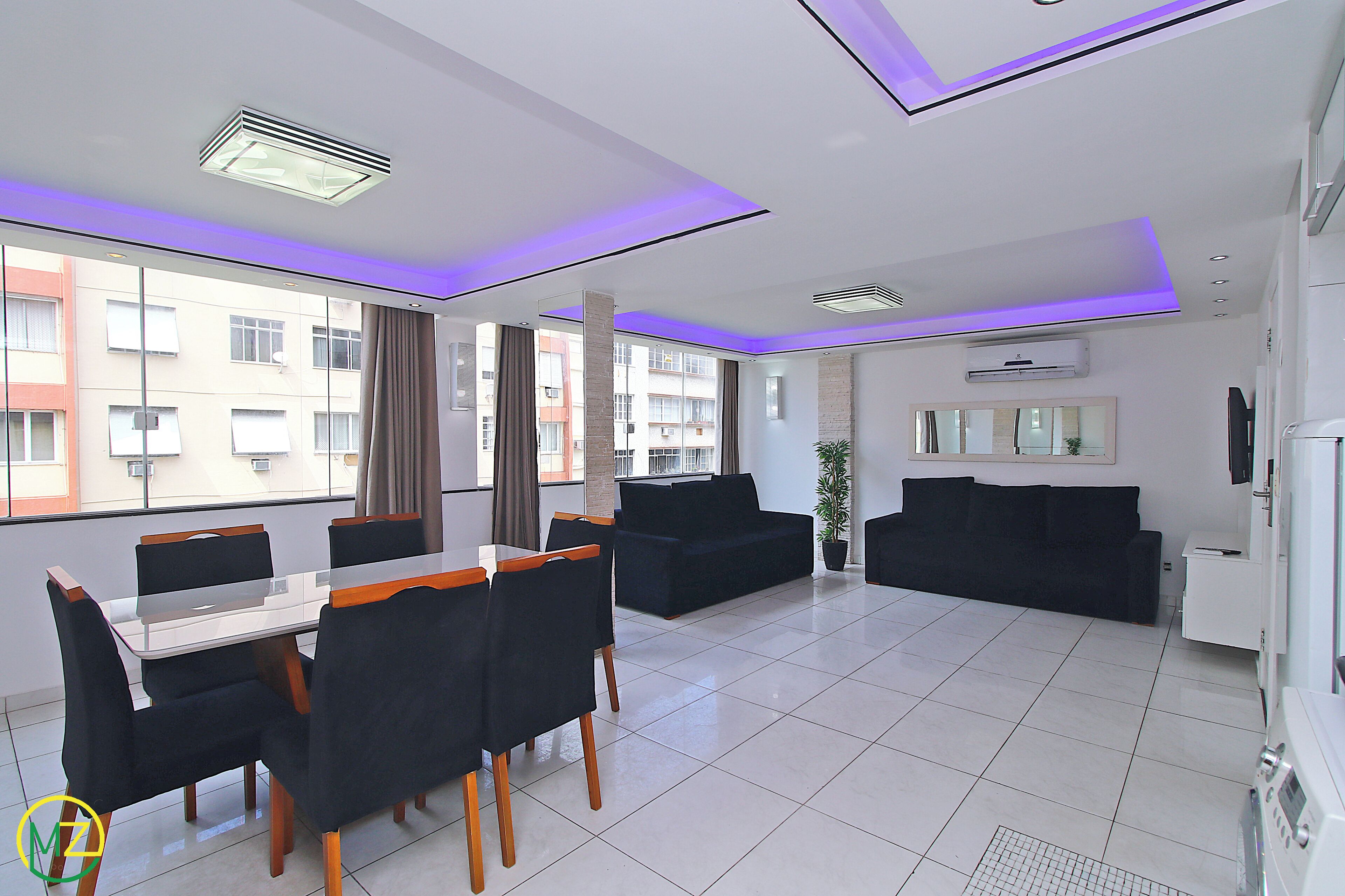 Una sala de estar moderna con comedor, que incluye un sofá, televisor y un amplio ventanal con cortinas.
