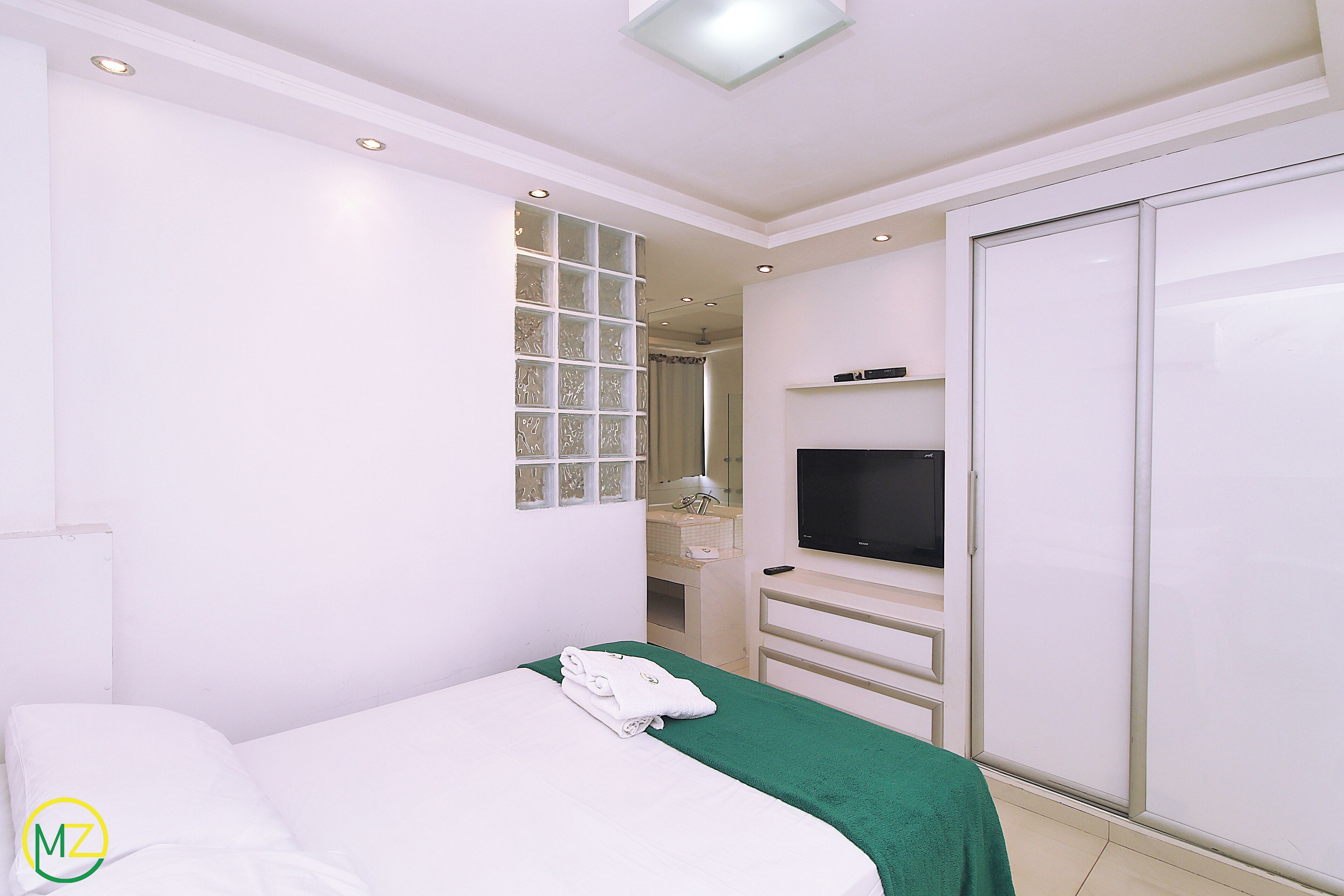 A hotel room with a bed, a TV, a wardrobe, and a bathroom visible through a glass door.