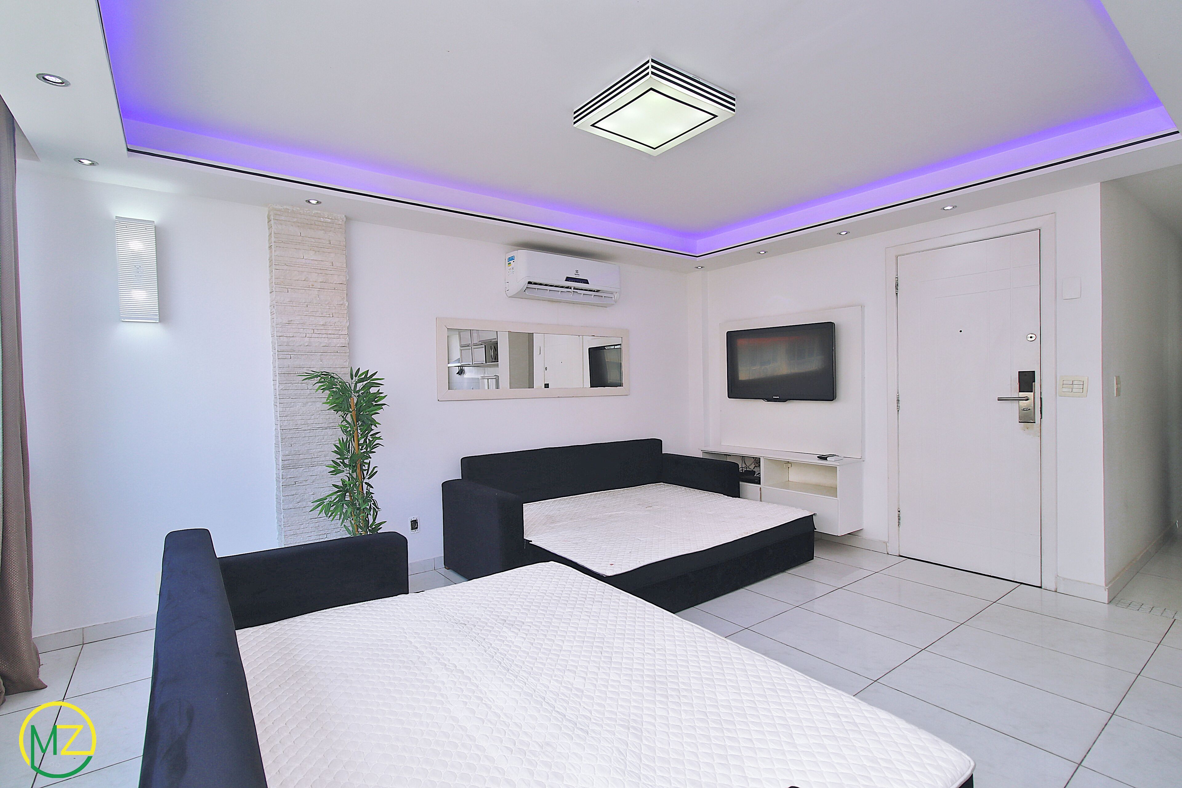 A modern bedroom with two beds, a TV, and an air conditioning unit.