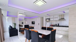 Una cocina moderna con armarios blancos, una estufa y un microondas. Hay una zona de comedor con una mesa blanca y sillas negras.