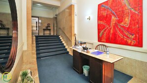 A hotel lobby with a staircase, a reception desk, and a large abstract painting on the wall. - MZapartments Prado II (Rio de Janeiro)