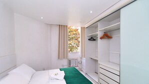 A hotel room with a bed, a green towel, a window with curtains, a radiator, and a wardrobe with a hanger. - MZapartments Prado II (Rio de Janeiro)