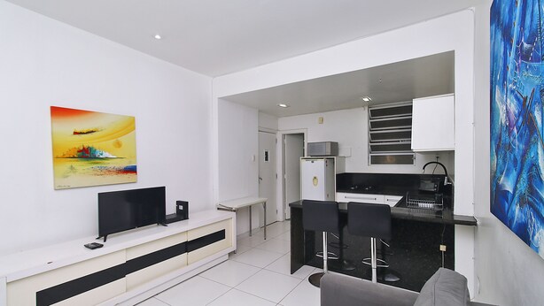 A modern living room with a flat-screen TV, a sofa, and a dining area with a bar. - MZapartments Prado II (Rio de Janeiro)